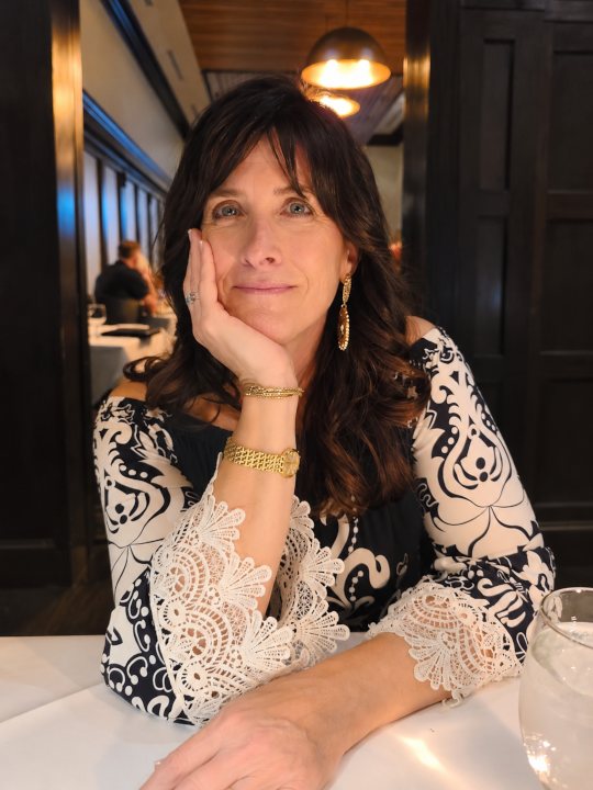 Kristen Bianchi, smiling in a white blouse with her hand resting against her cheek.